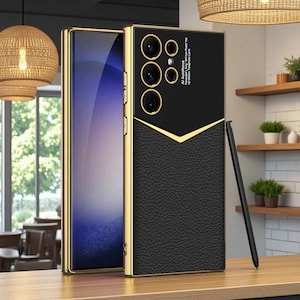 May include: A black smartphone case with a textured leather-like lower section and a smooth upper panel featuring camera cutouts and the text AI Autofocus. The case has gold-coloured metallic edges and is accompanied by a slim black stylus pen.