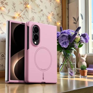 Puede incluir: Una funda para smartphone plegable de color rosa claro con un anillo de carga magnético circular en la parte posterior, un módulo de cámara vertical con dos lentes y la marca Abeel impresa cerca del borde inferior de la funda de silicona.