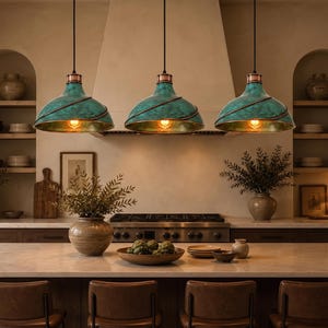 May include: Three pendant lights featuring wide, dome-shaped shades with a textured, oxidized teal green finish and copper-toned spiral accents. Each light hangs from a black cord and emits a warm, glowing light from a visible filament bulb.