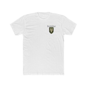 May include: A white short-sleeve t-shirt featuring a small green shield emblem on the left chest. The shield displays a white oak leaf design, and the word Semine is printed in black text above the shield in a classic serif font style.