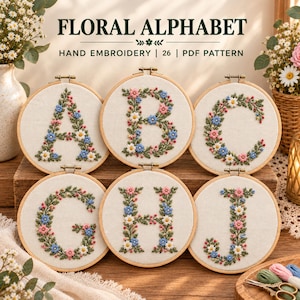 May include: Six circular wooden embroidery hoops containing fabric with hand-stitched floral letters A, B, C, G, H, and J. The text "FLORAL ALPHABET HAND EMBROIDERY | 26 | PDF PATTERN" is displayed above the hoops on a light background.