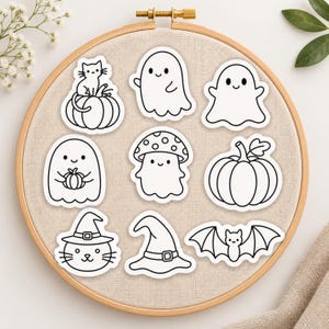 May include: A set of eight black and white stickers arranged on a round wooden embroidery hoop. The stickers feature line art illustrations of a cat on a pumpkin, two ghosts, a ghost holding a pumpkin, a mushroom, a pumpkin, a cat in a witch hat, a witch hat, and a bat.