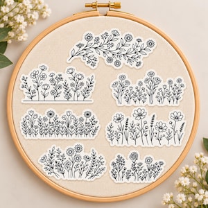 May include: Six distinct black and white floral stickers arranged on a light beige fabric background inside a wooden embroidery hoop. Each sticker features a unique line art illustration of various wildflowers, stems, and leaves.