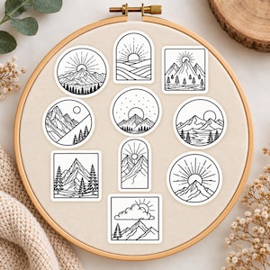 May include: A collection of ten black and white stickers featuring line art illustrations of mountain landscapes, pine trees, sunbursts, and clouds. The stickers are arranged on a circular wooden embroidery hoop frame with a light fabric background.