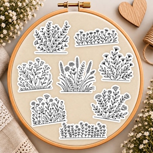 May include: A collection of eight black and white stickers featuring various botanical illustrations of wildflowers, grasses, and floral clusters arranged on a circular wooden embroidery hoop with a light beige fabric background.