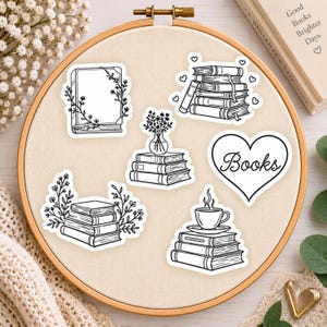 May include: A collection of six black and white vinyl stickers featuring book-themed illustrations, including stacks of books, a floral book frame, a heart shape with the text Books, and a cup of coffee, all arranged on a circular embroidery hoop.