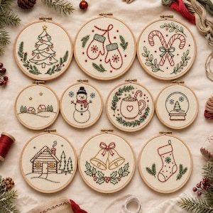 May include: Ten circular embroidery hoops featuring holiday designs on cream fabric. Patterns include a Christmas tree, mittens, candy canes, a snowy landscape, a snowman, a mug of cocoa, a snow globe, a cabin, bells, and a Christmas stocking.
