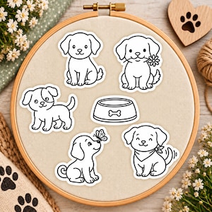 May include: A set of five black and white stickers featuring four puppies and one dog bowl, arranged on a circular wooden embroidery hoop. The designs include a puppy sitting, a puppy holding a flower, a puppy standing, a puppy with a butterfly, and a puppy wearing a bandana.