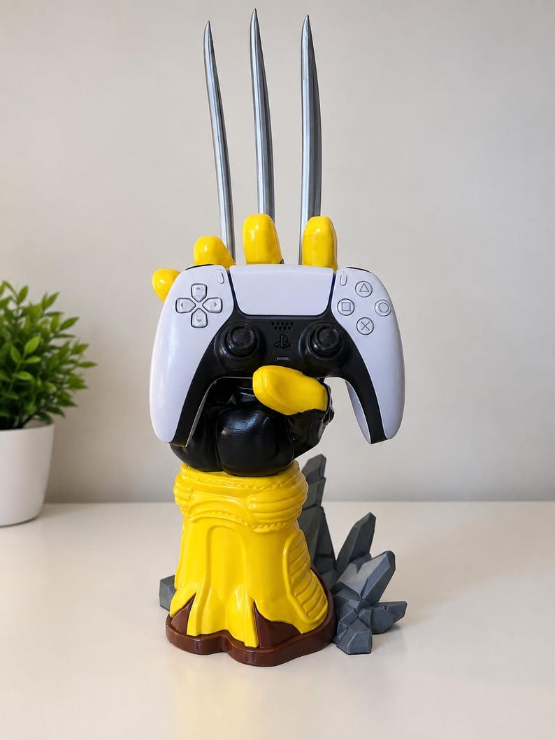May include: A yellow and black hand-shaped controller stand featuring three long silver metallic claws extending upwards from the knuckles. The stand holds a white and black wireless game controller with standard directional buttons and analogue sticks.