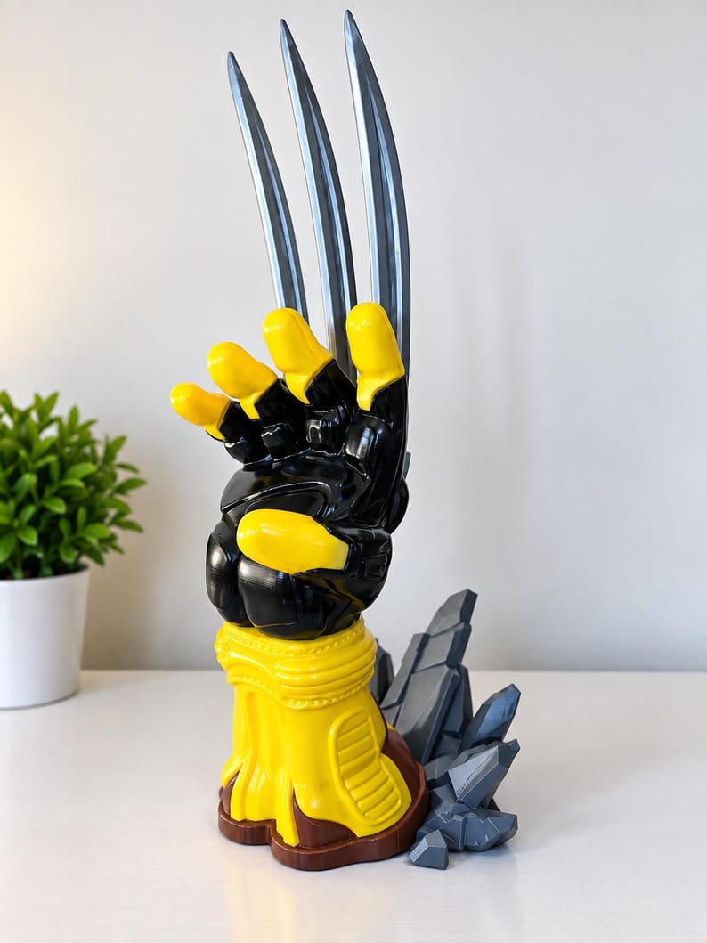 May include: A sculpted hand figurine featuring a glossy black and yellow colour scheme with three long, silver-coloured metallic blades extending from the knuckles. The base is yellow with brown accents, supported by a cluster of jagged, grey rock-like structures.