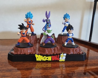 May include: A set of five Dragon Ball Super character figurines displayed on a brown rocky base. The figures include Goku, Vegeta, and Beerus, each in a distinct pose. The black base features the yellow and red Dragon Ball Super logo text.