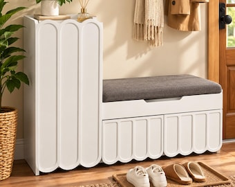 May include: A white entryway storage bench featuring a tall cabinet section and a lower bench seat with a dark gray upholstered cushion. The unit has vertical scalloped detailing on the cabinet door and two lower drawer fronts.
