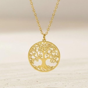 May include: A gold-colored necklace featuring a circular pendant with a detailed tree of life design. The pendant is suspended from a delicate chain. The necklace is displayed against a neutral background, highlighting its intricate details.