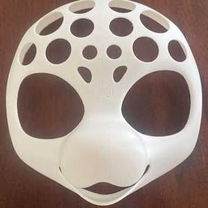May include: A white, dome-shaped, 3D-printed mask base with a smooth finish. The structure features a series of circular cutouts of varying sizes across the upper portion, with two large, symmetrical openings on the sides and a solid nose section.