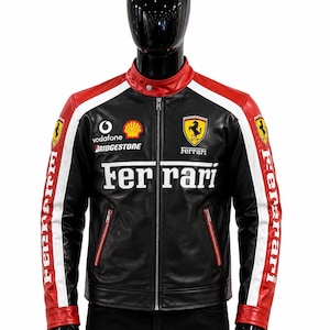 May include: A black leather jacket featuring red and white accents on the sleeves and shoulders. The front displays the Ferrari logo, the word Ferrari, and sponsor logos for Vodafone, Shell, and Bridgestone. It has a stand-up collar and zip fastening.
