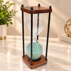 May include: An hourglass featuring a clear glass bulb filled with light green sand, held within a frame of four black metal rods and square wooden top and bottom plates. The structure is supported by small black feet at each corner of the base.