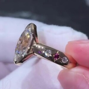 Bague de fiançailles en or massif 14 carats, sertie d'une moissanite ovale et d'un rubis en étoile, ornée d'un diamant. Un cadeau d'anniversaire unique.