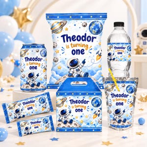 May include: A collection of space-themed party favors featuring a blue and white design with planets, stars, and an astronaut. Each item displays the text "Theodor is turning one" and includes a chip bag, water bottle, juice pouch, and candy wrappers.