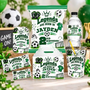 May include: A collection of football-themed party supplies featuring the text Legends Are Born In Jayden 2nd Birthday, including a crisp packet, water bottle, juice pouch, snack wrappers, and a treat box, all decorated with green football graphics.