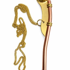 Pu&ograve; includere: Un fischietto da nostromo in rame e ottone, caratterizzato da un tubo curvo, una catena in metallo dorato e una boa sferica con un emblema a ancora in rilievo. Il fischietto presenta due anelli decorativi in ottone che fissano il tubo di rame.