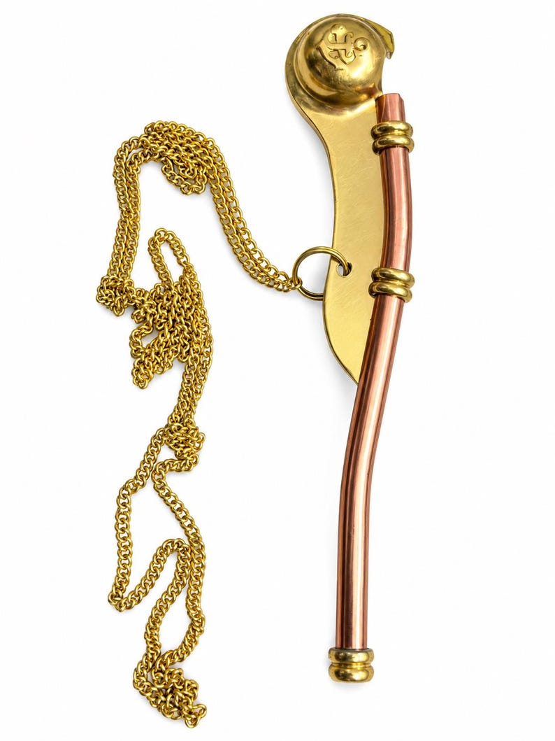 Pu&ograve; includere: Un fischietto da nostromo in rame e ottone, caratterizzato da un tubo curvo, una catena in metallo dorato e una boa sferica con un emblema a ancora in rilievo. Il fischietto presenta due anelli decorativi in ottone che fissano il tubo di rame.