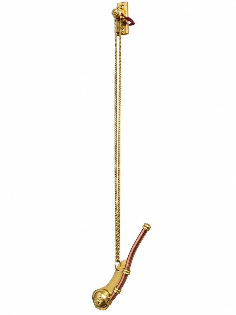 Pu&ograve; includere: Un gancio da parete in metallo dorato con una piastra di montaggio rettangolare verticale e un lungo braccio curvo. Una sottile catena dorata pende dal supporto superiore, collegata a un ornamento decorativo in metallo color rame e oro a forma di fischietto.