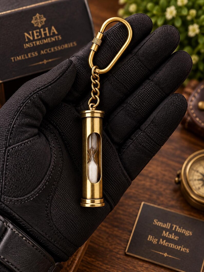 May include: A brass hourglass keyring featuring a cylindrical metal frame with a clear glass centre containing white sand. The hourglass is attached to a brass chain and a carabiner-style clip, designed for portability and functional timekeeping.