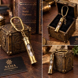 May include: A brass hourglass keyring featuring a cylindrical metal frame with a glass centre containing white sand. The keyring is attached to a brass carabiner and is presented with a square, antique-style box and a black card labelled NEHA INSTRUMENTS.