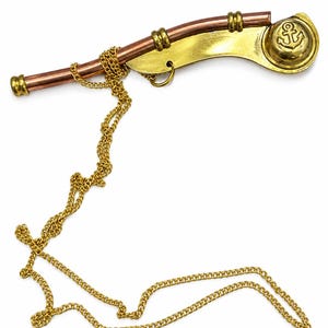 Pu&ograve; includere: Un fischietto da nostromo in rame e ottone lucidato, caratterizzato da un design curvo con una catena in metallo dorato attaccata. Il fischietto include un tappo circolare in ottone con impresso un simbolo di ancora, riflettendo un'estetica nautica.