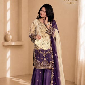 Könnte beinhalten: Ein dreiteiliges Set in Creme und Dunkelviolett, bestehend aus einer langärmeligen Tunika mit Goldstickerei, einer passenden weiten Hose und einem transparenten Dupatta. Das Kyora Couture Logo ist oben rechts im Bild zu sehen.