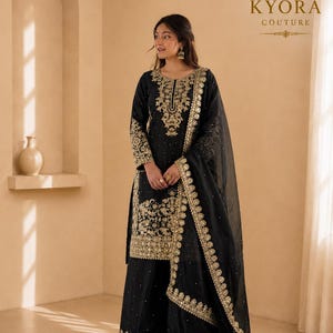 May include: A black salwar kameez set featuring intricate gold embroidery on the neckline, sleeves, and hem. The outfit includes a matching black dupatta with a wide gold embroidered border and scattered gold accents throughout the fabric.