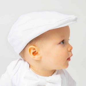 May include: A white baby hat with a flat top and a brim. The hat is made of a soft, lightweight fabric.