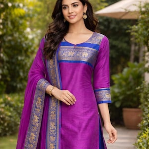May include: A vibrant magenta and blue salwar kameez featuring a round neckline, three-quarter sleeves, and a matching dupatta. The garment is adorned with a gold and blue woven border pattern that includes repeating elephant motifs along the chest.