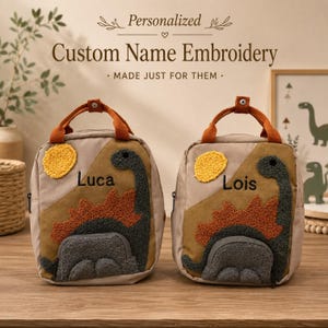 May include: Two beige backpacks featuring textured dinosaur appliques in dark gray and rust orange, with a yellow sun. Each bag has a top handle and is embroidered with the names Luca and Lois. The text Personalized Custom Name Embroidery is visible.