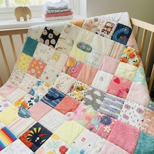 Könnte beinhalten: Eine Patchwork-Decke aus verschiedenen Stoffquadraten mit unterschiedlichen Mustern wie Blumen, Herzen, Walen, Dinosauriern und britischen Flaggen. Ein Quadrat enthält den gestickten Text "love my daddy" in hellblauer Schreibschrift.