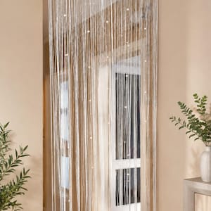 May include: A white string curtain featuring a woven header and thin, vertical strands interspersed with small, round, white beads. The curtain hangs from the top of a doorway, creating a semi-transparent partition with a delicate, linear texture.