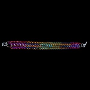 Pode incluir: Uma pulseira de malha de aço com um gradiente de arco-íris vibrante de anéis metálicos entrelaçados. As cores transitam suavemente do vermelho e roxo escuro nas extremidades para o azul, verde e amarelo brilhante no centro. Fecho de barra.