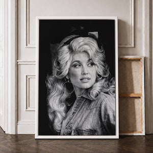 May include: A black and white portrait print of a person with voluminous, wavy blonde hair styled with a headband. The subject is wearing a collared denim shirt and large hoop earrings, captured in a three-quarter view against a dark background.