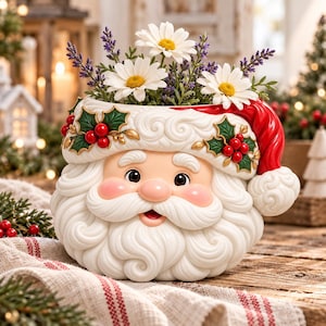 Pode incluir: Um vaso de cerâmica em forma de cabeça de Pai Natal com barba branca encaracolada, gorro vermelho com pompom branco e detalhes de azevinho. O vaso está cheio de margaridas brancas e ramos de alfazema, criando um arranjo festivo.