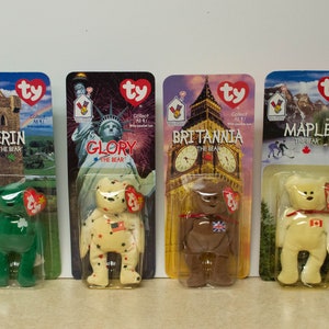 May include: Four Ty Beanie Babies, each representing a different country. Erin the Bear is green and has a shamrock on its chest. Glory the Bear is cream with red stars and a US flag on its chest. Britannia the Bear is brown with a Union Jack on its chest. Maple the Bear is cream with a Canadian flag on its chest.