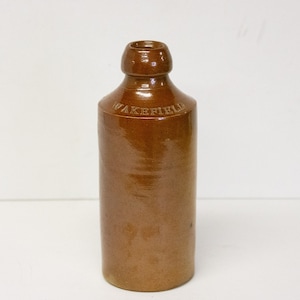 May include: A brown ceramic bottle with a rounded top and a label that reads "WAKEFIELD".