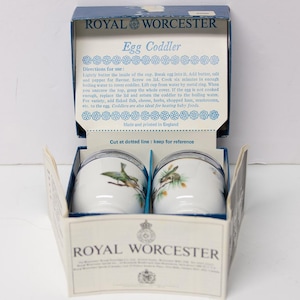May include: Royal Worcester Egg Coddler set in its original box. The white ceramic egg coddlers feature a bird and branch design. The box is blue and white with the Royal Worcester logo and instructions.