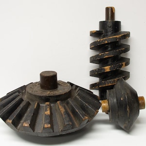 May include: Three antique wooden gears with a dark finish. The gears include a large cogwheel, a spiral gear, and a conical gear. The wood shows signs of age and wear, with exposed lighter wood.