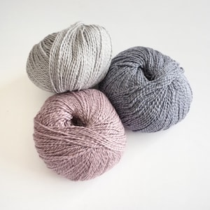May include: Three balls of yarn in different shades of grey, pink, and blue. The yarn is soft and fluffy, perfect for knitting or crocheting.