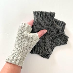 May include: Two pairs of fingerless gloves, one gray and one white, made of crocheted yarn.