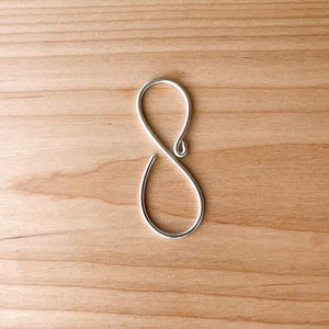 May include: A silver-colored, infinity-shaped hook. The hook is made of metal and has a smooth finish.