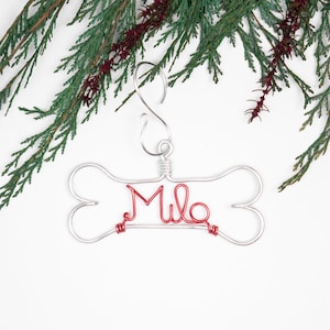 May include: A silver wire dog bone ornament with the name "Milo" written in red wire.