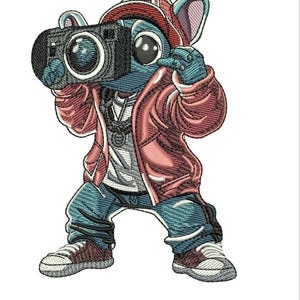 May include: An embroidered patch featuring a blue cartoon character wearing a red baseball cap, a red jacket, and blue jeans. The character is holding a black camera up to its face with both hands and wearing white sneakers with brown accents.