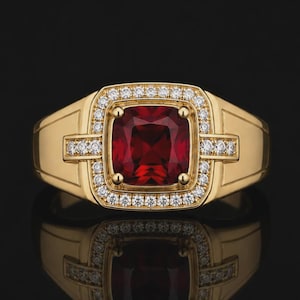 Peut inclure: Une bague en or avec une grande pierre précieuse rouge foncé de taille carrée au centre. La pierre est entourée d'un halo de petites pierres blanches rondes et transparentes. D'autres petites pierres blanches ornent l'anneau en or.