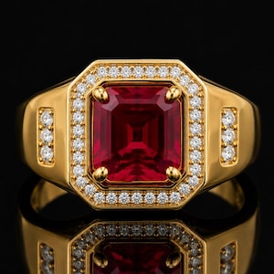 Puede incluir: Un anillo de oro con una gran piedra preciosa rectangular de color rojo intenso en el centro. La piedra está rodeada por un halo de pequeñas piedras redondas transparentes. Tres piedras pequeñas y transparentes están engastadas verticalmente a cada lado.